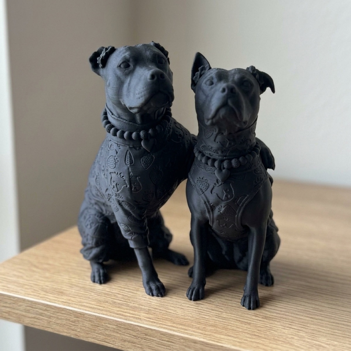The same two dogs sculpted in midnight black, standing straight on a wooden shelf