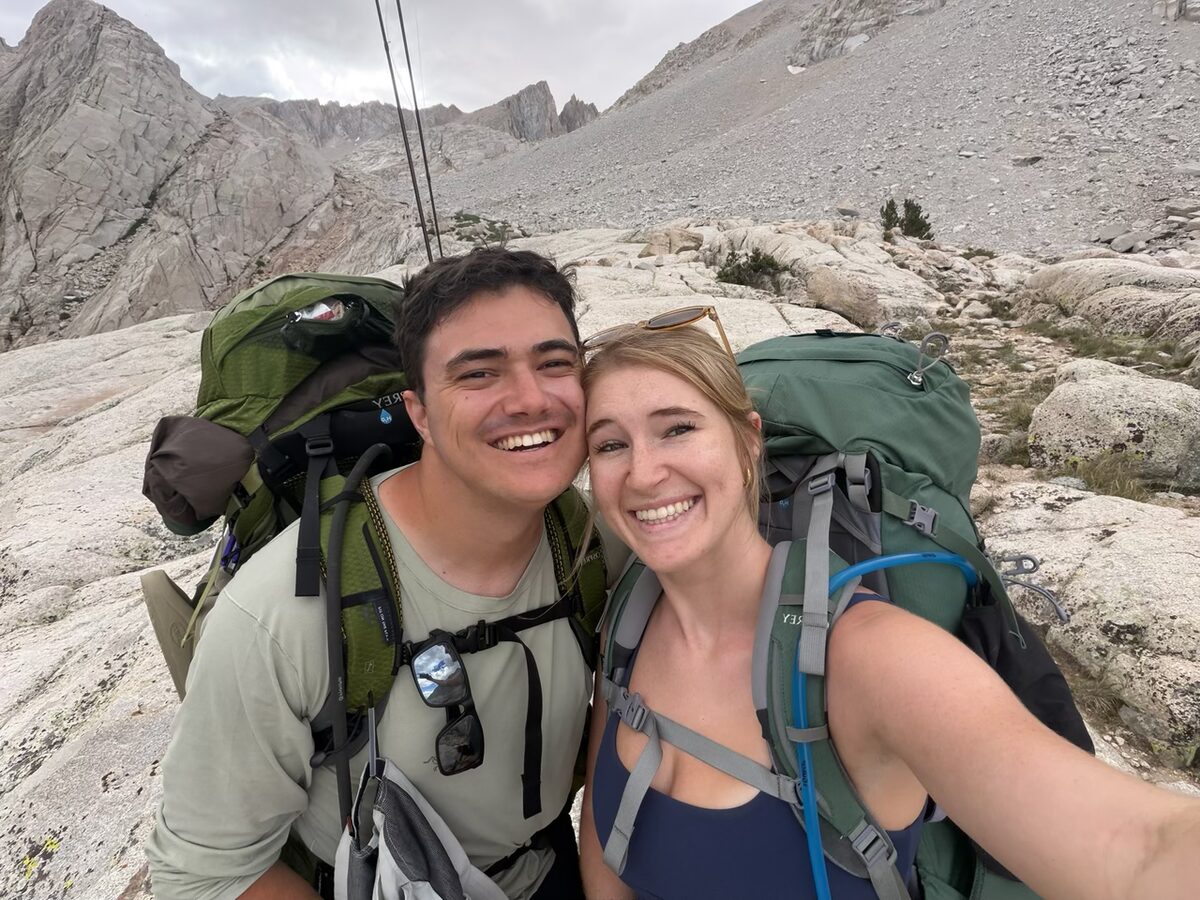The two of us smiling on a mountain hike, backpacks on